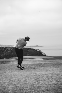 A golfer mid-swing with a scenic backdrop of rolling hills and a clear blue sky.