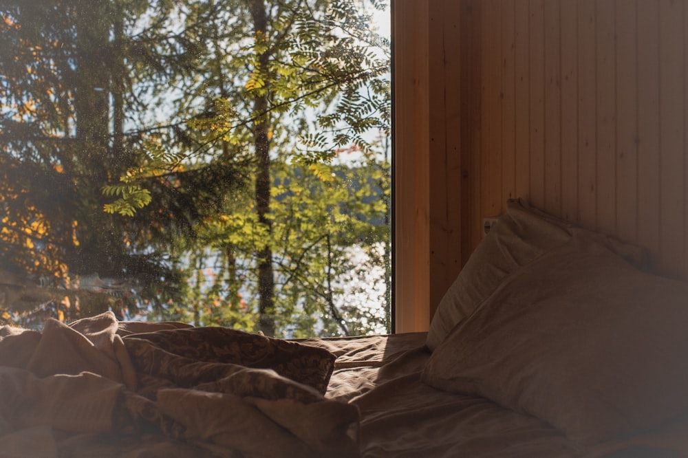 an unmade bed with a view of a forest