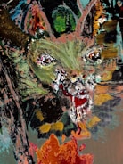 An abstract painting featuring a central cat-like face with intense, wide eyes and an open mouth, possibly with fangs. The strokes are bold and chaotic, using a mix of greens, reds, and browns. The surrounding area features abstract shapes and colors, giving the image a slightly menacing or eerie quality.