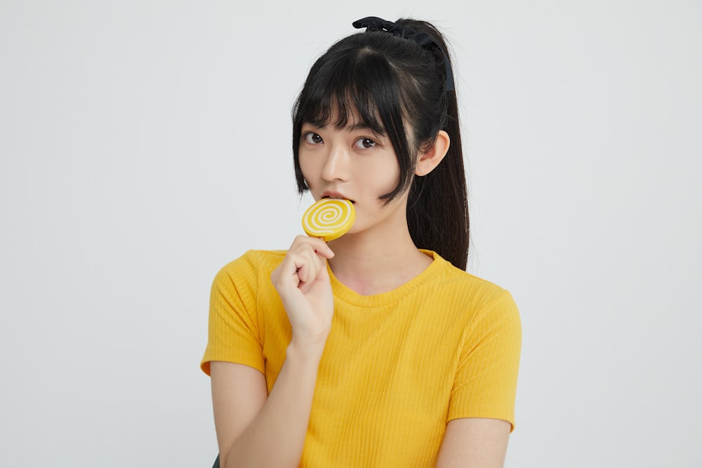 a woman in a yellow shirt eating a lollipop