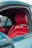 The interior of a car features vibrant red leather seats against a backdrop of a neutral-toned car exterior. The door frame and window are visible, with a glimpse of a vehicle parked beside it.