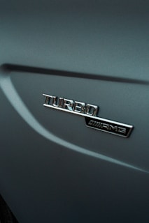 An emblem displaying the word 'Turbo' alongside an AMG logo on a metallic car surface, with smooth curves and a glossy finish.