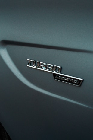 An emblem displaying the word 'Turbo' alongside an AMG logo on a metallic car surface, with smooth curves and a glossy finish.