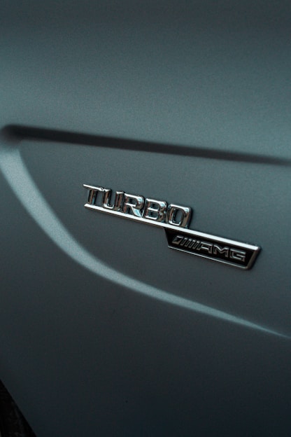 An emblem displaying the word 'Turbo' alongside an AMG logo on a metallic car surface, with smooth curves and a glossy finish.
