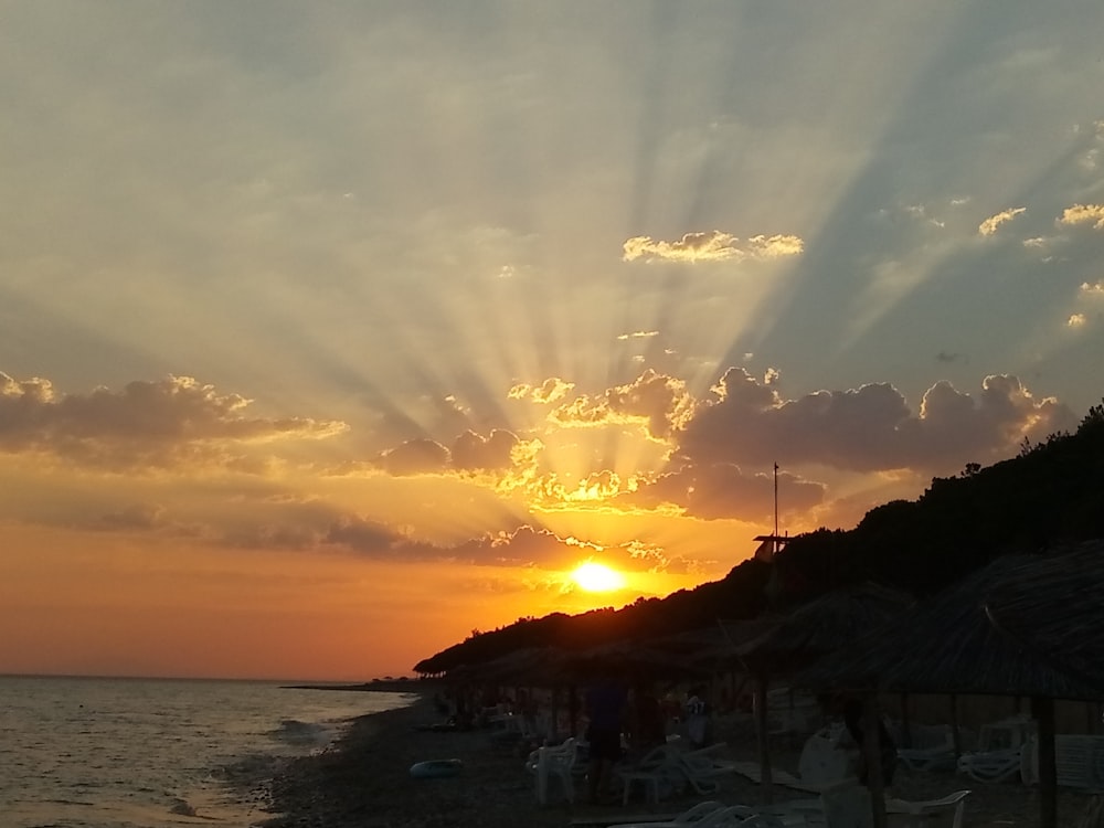 the sun is setting over a beach with umbrellas