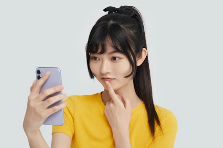 A smiling teenager holding a phone, looking thoughtful and peaceful in a sunlit room.