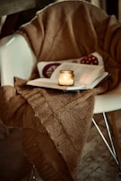 A cozy corner with a knitted blanket draped over a chair beside a softly glowing lamp.
