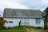A large old barn with a weathered roof and a white exterior, featuring a mural of colorful flowers and the text 'Clinton County 1810-2010'. Greenery surrounds the barn, and a small window with shutters is visible on the side.