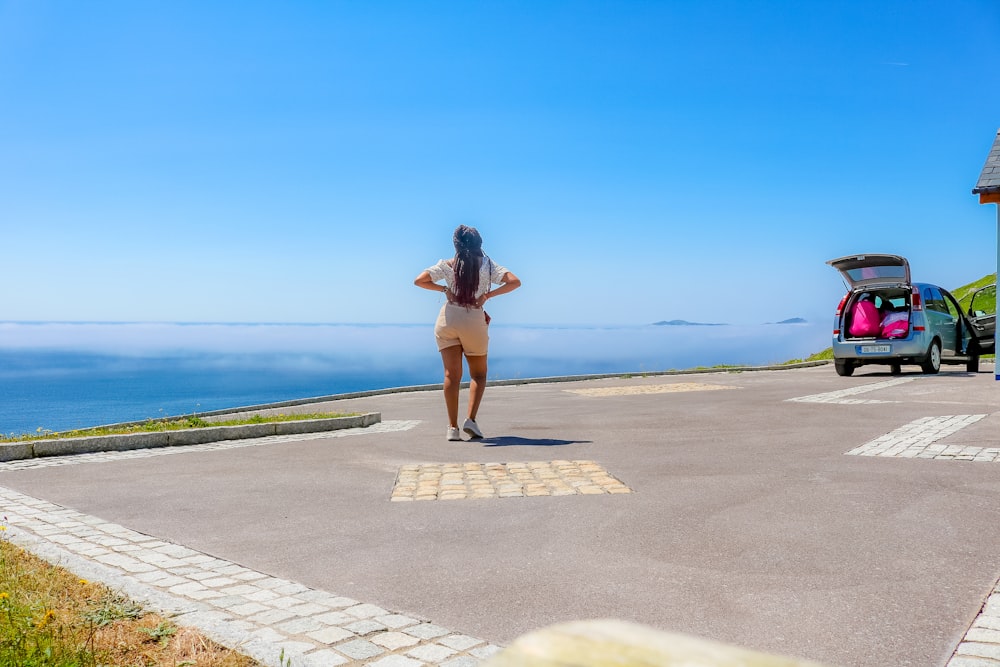 a woman standing in a parking lot next to a car