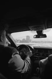 Close-up of a driver’s hand holding a steering wheel with a cityscape in the background.