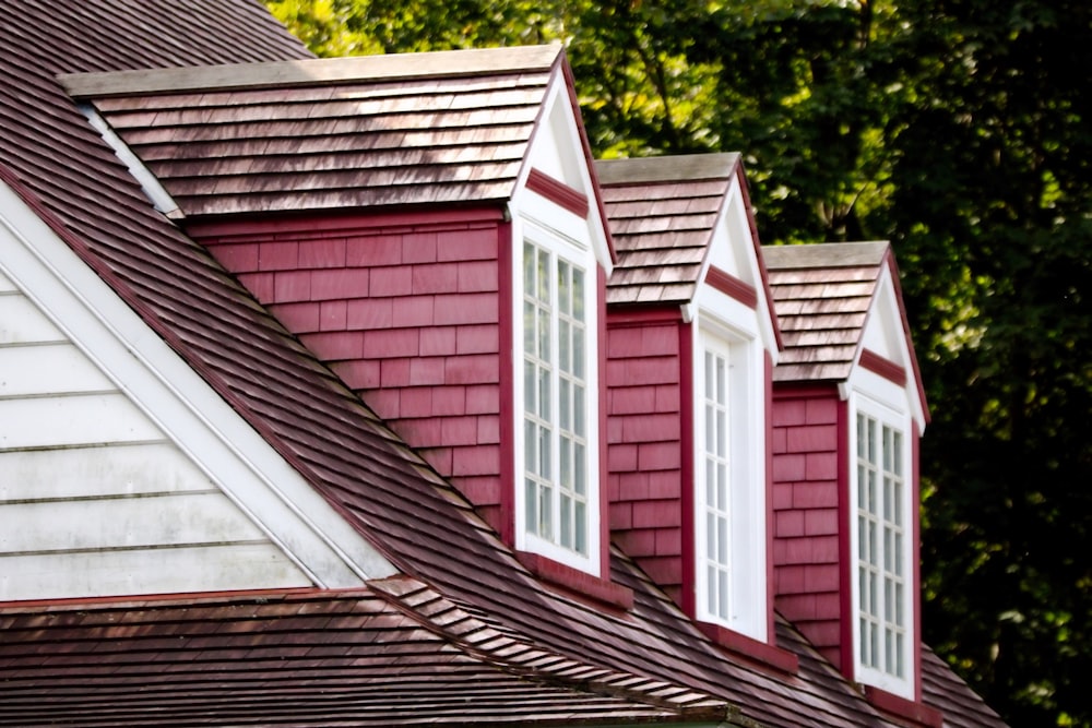 a red house with three white windows and a brown roof