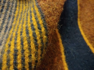 A close-up view of a textured fabric featuring alternating stripes of yellow and dark blue. The fabric appears soft with visible fibers and a fuzzy surface.