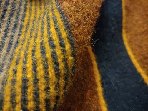 A close-up view of a textured fabric featuring alternating stripes of yellow and dark blue. The fabric appears soft with visible fibers and a fuzzy surface.