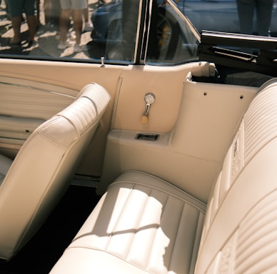 A vintage car interior featuring beige leather seats and a classic design. The upholstery is in pristine condition, evoking a sense of elegance and nostalgia. Sunlight streams through the windows, casting warm shadows.