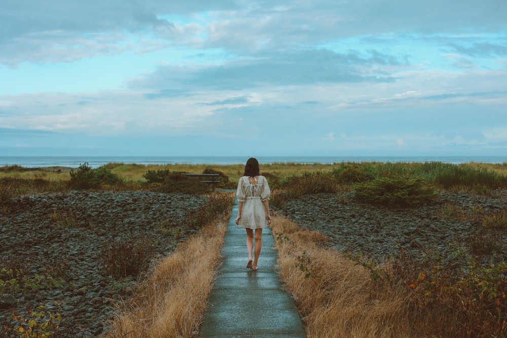 a woman in a white dress walking down a path