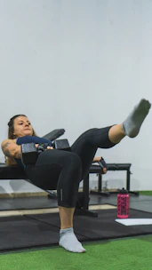 Woman exercising at home using a broomstick and water bottles as workout tools.
