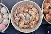 A collection of various artisanal bread rolls and pastries is arranged in woven baskets. The breads have distinct textures and appearances, ranging from twisted designs to intricately baked patterns.