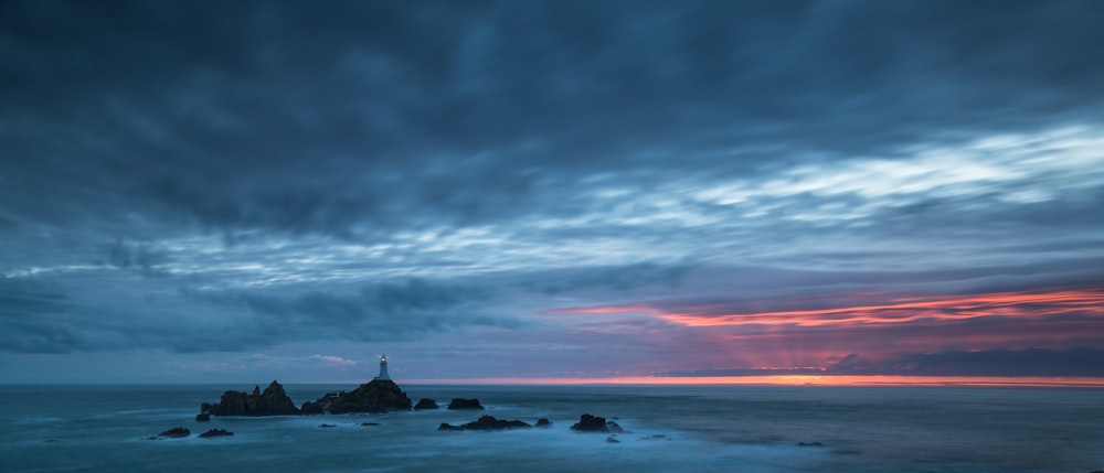 a lighthouse sitting on top of a rocky beach under a cloudy sky