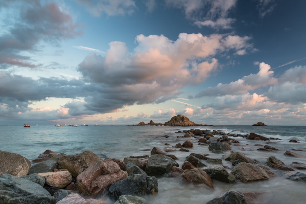 a beach with rocks and water under a cloudy sky