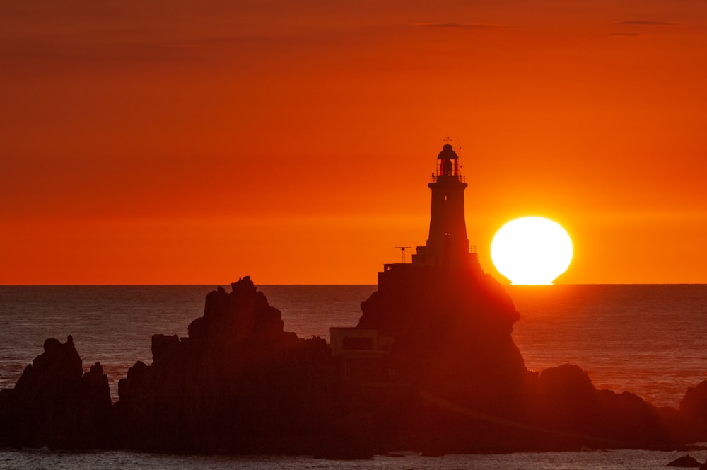 the sun is setting over the ocean with a lighthouse in the foreground
