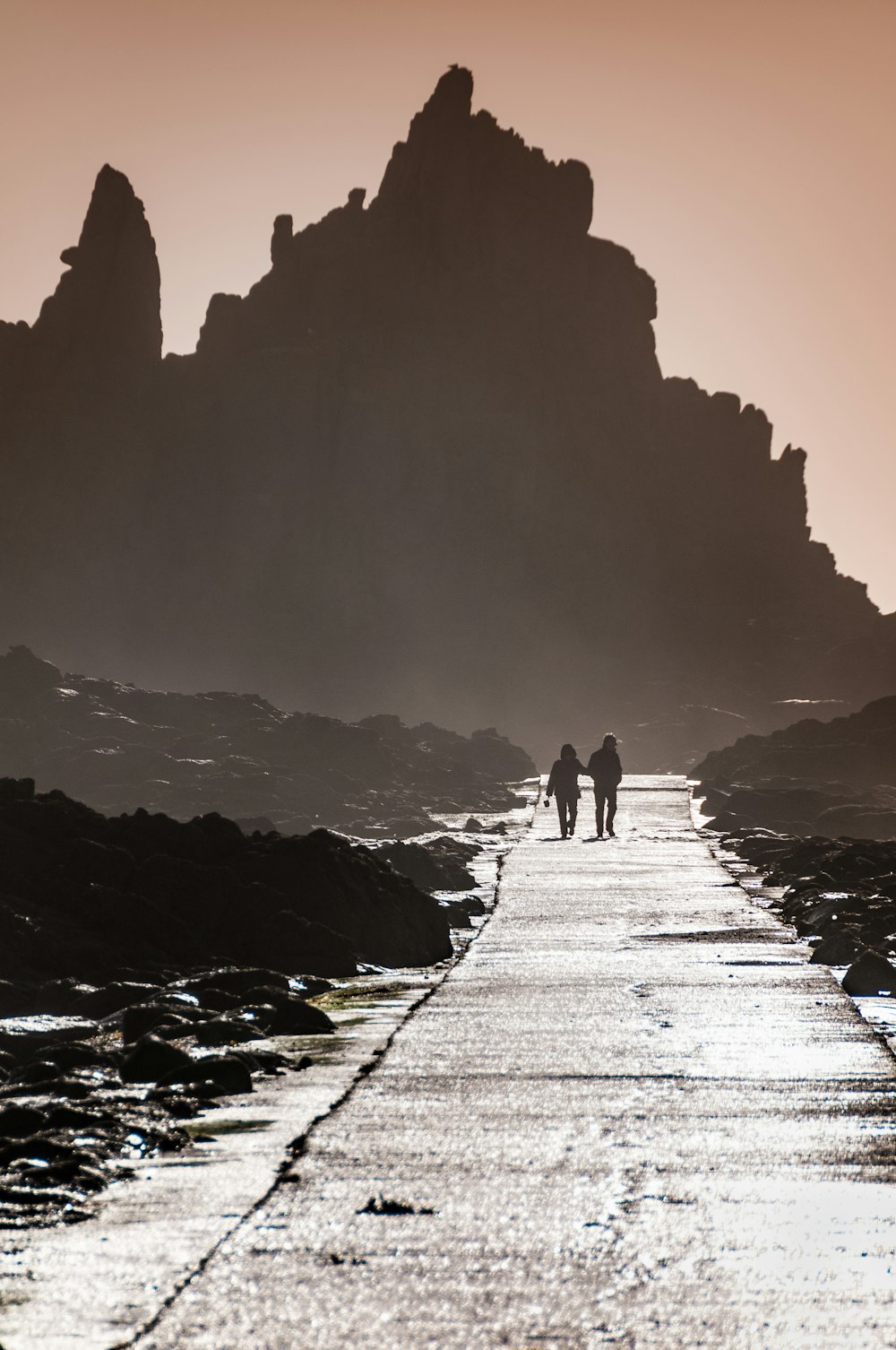 a couple of people walking down a road next to the ocean