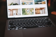 A close-up view of an open laptop showing a photo gallery on its screen, with a focus on the keyboard which is dimly lit. The background images on the screen appear blurred.