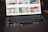 A close-up view of an open laptop showing a photo gallery on its screen, with a focus on the keyboard which is dimly lit. The background images on the screen appear blurred.