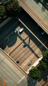 An aerial view of a highway with multiple lanes, where a few vehicles such as cars and a truck are visible. Bridges create shadows on the road, and trees are present at the edges of the road.