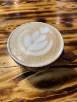 Close-up of a latte art heart atop a creamy coffee in a sleek ceramic cup on a wooden table.