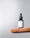 A black dropper bottle labeled 'Minimalist Retinol 0.5%' sits on a wooden shelf against a light gray background. The design is simple and modern, emphasizing the minimalist branding.