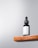 A black dropper bottle labeled 'Minimalist Retinol 0.5%' sits on a wooden shelf against a light gray background. The design is simple and modern, emphasizing the minimalist branding.
