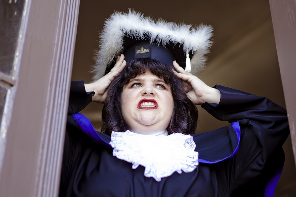 a woman in a graduation gown holds her hat over her head