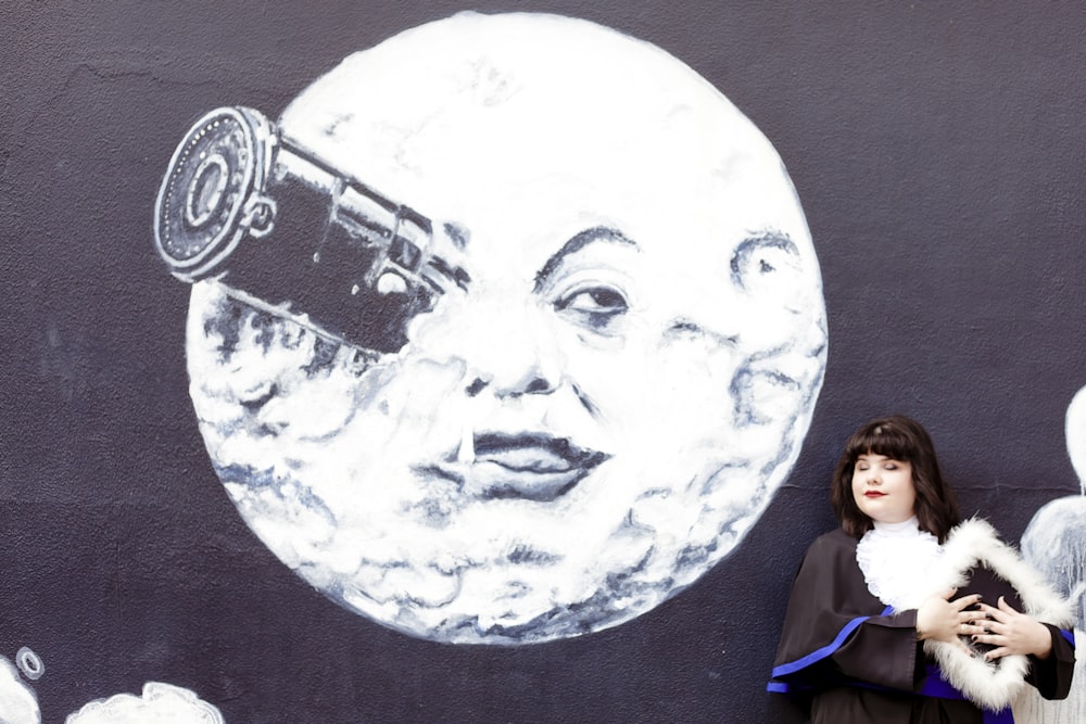 a woman standing in front of a wall with a mural of a moon and a