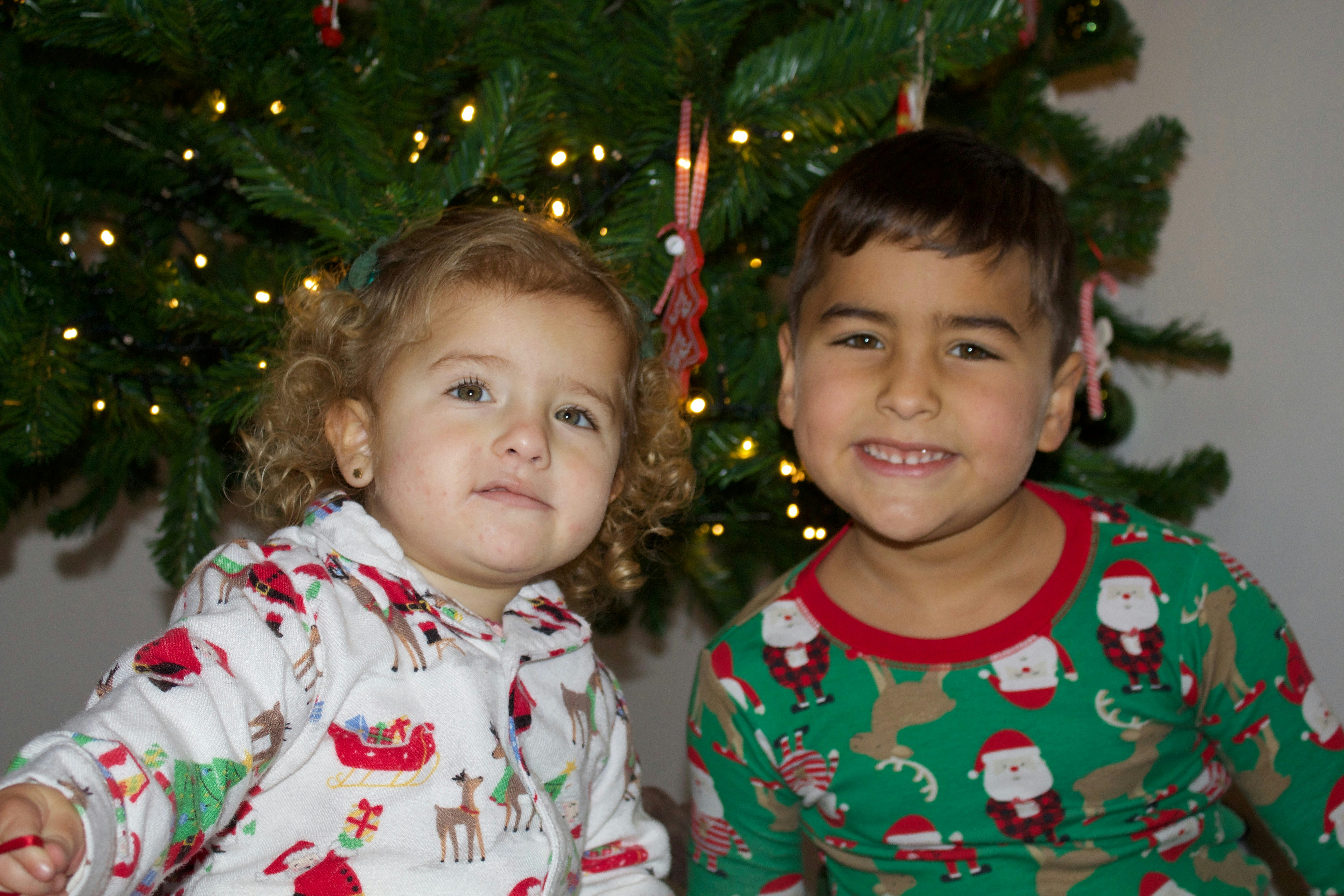 a couple of kids standing next to a christmas tree