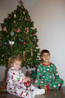 Smiling children dressed in holiday pajamas reading by a Christmas tree.