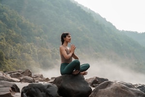 a woman sitting on top of a rock next to a river