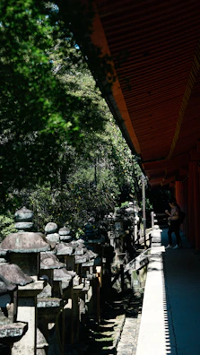 Visitors walking along a shaded path lined with stone lanterns and natural foliage.