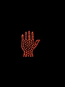 A digital stop sign in the shape of a hand is made up of numerous red LED lights against a dark background. The hand symbol is illuminated, clearly signaling to stop.