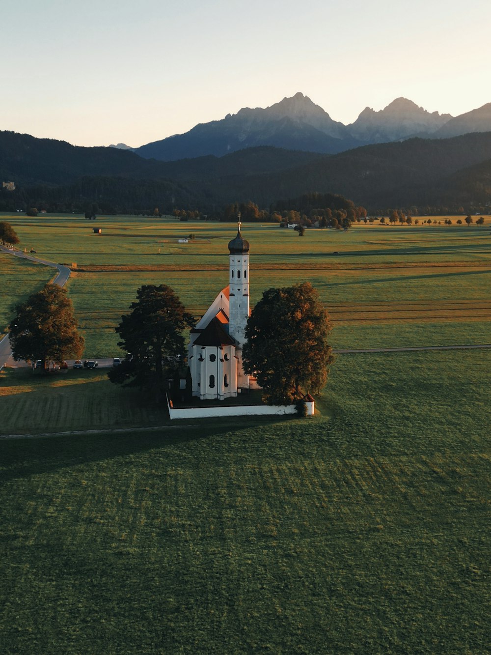 a church in the middle of a field with mountains in the background