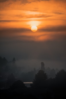 the sun is setting over a foggy city