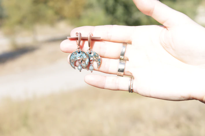 Close-up of colorful turquoise and silver earrings reflecting sunlight on a sandy beach