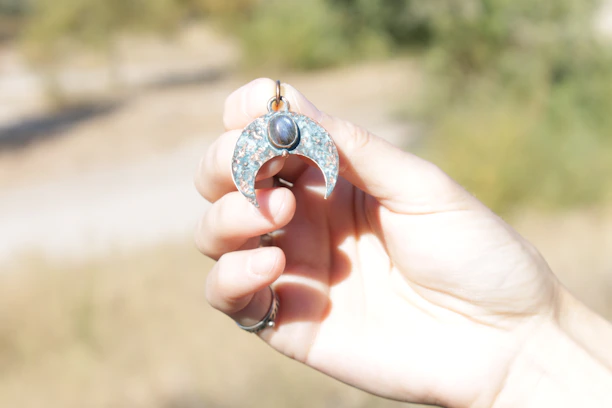 A close-up of a hand holding a shimmering copper amulet against a deep blue night sky.