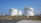 Several large, industrial storage tanks are situated on a grassy area, equipped with safety railings and exterior staircases. These tanks are part of a storage facility under a clear blue sky.