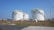 Several large, industrial storage tanks are situated on a grassy area, equipped with safety railings and exterior staircases. These tanks are part of a storage facility under a clear blue sky.