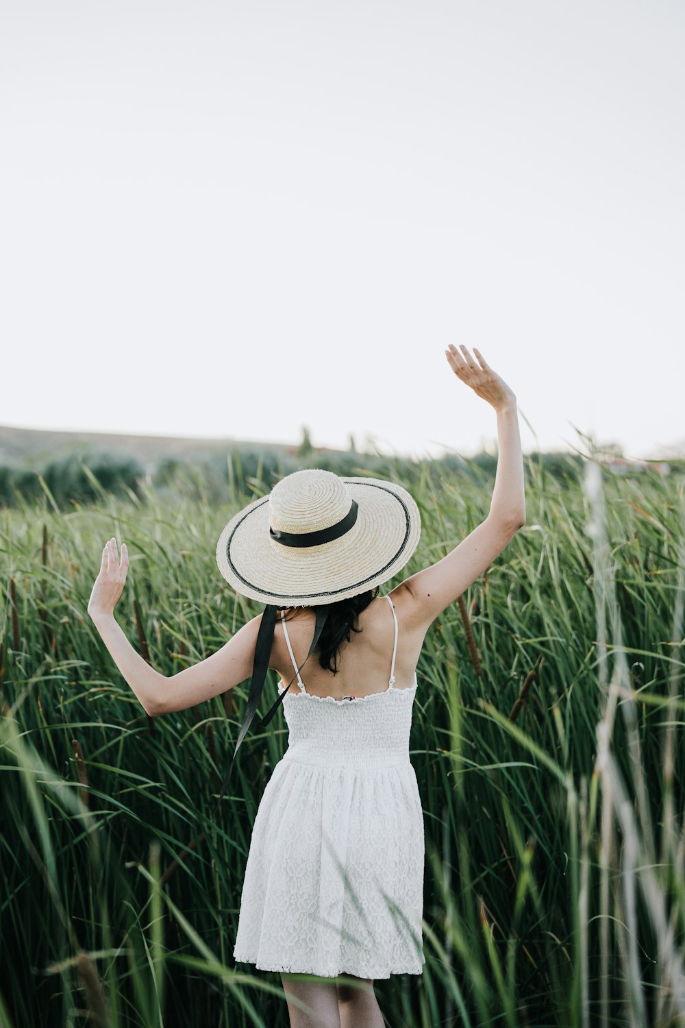 a woman in a white dress and hat standing in tall grass