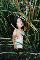 A model wearing earthy-toned makeup with terracotta eyeshadow and a soft matte brown lip, posing against a backdrop of tall prairie grass.