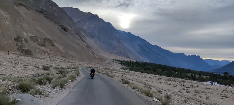 A lone rider cruising a winding mountain road at dusk, the sky painted in deep charcoal and bronze hues.