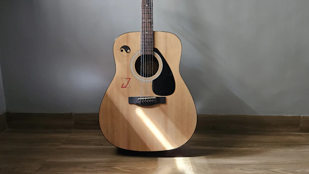 Close-up of an acoustic guitar resting against a rustic wooden wall, bathed in soft sunlight.