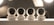 Four white security cameras are lined up on a surface with soft studio lighting in the background. Each camera is identical in design, with a spherical shape and a black lens visible in the front. The lighting creates a muted, professional atmosphere.