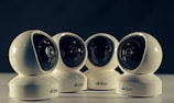 Four spherical security cameras with a glossy white finish are positioned in a row, each featuring a prominent lens and the brand name 'Briton' visible on their bases. The background is dark, contrasting with the brightly lit cameras.